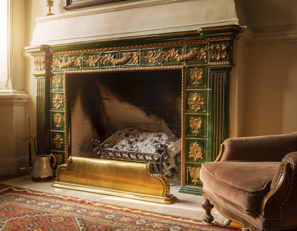 A hearth where the fire has gone out, the room still warm and lit from a window.